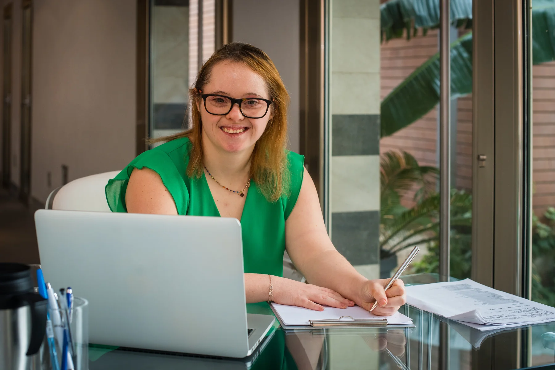 A girl smiling while writing in the front of a laptop